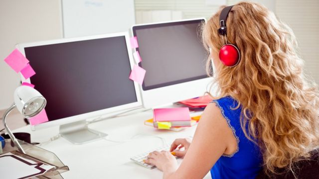 Una mujer frente a dos pantallas de computadora.