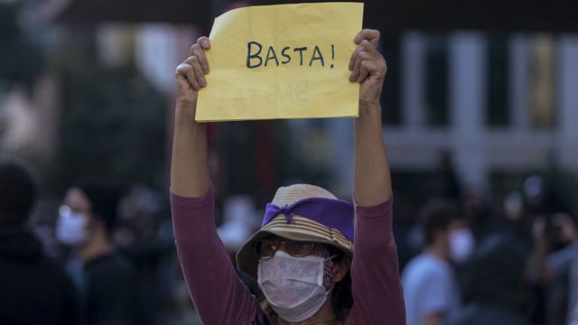Mulher de chapéu e máscara segura cartaz dizendo 'basta' na Avenida Paulista