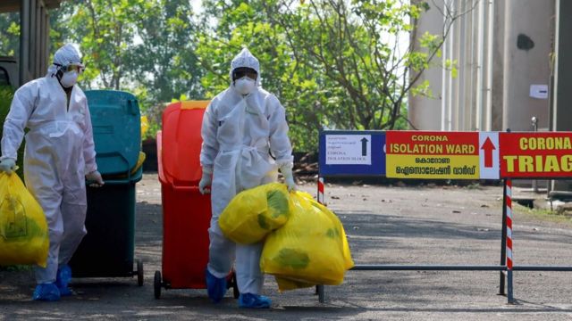 Des fonctionnaires de la santé portant des vêtements de protection transportent des déchets médicaux hors d'une salle d'isolement de l'Ernakulam Medical College à Kochi, en Inde