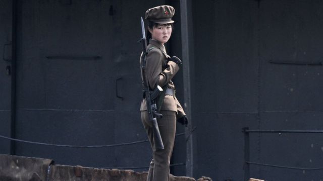 North Korean female officer in green uniform and gun looks at camera