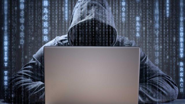 Un hacker trabajando en una laptop, con un sweater con capucha