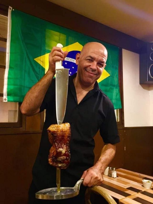 Sandro Pereira, brasileiro que vive na província de Hokkaido, onde foi registrado um forte terremoto no Japão, posa para foto segurando carne e uma faca, com uma bandeira do Brasil ao fundo. Ele trabalha em uma churrascaria na província