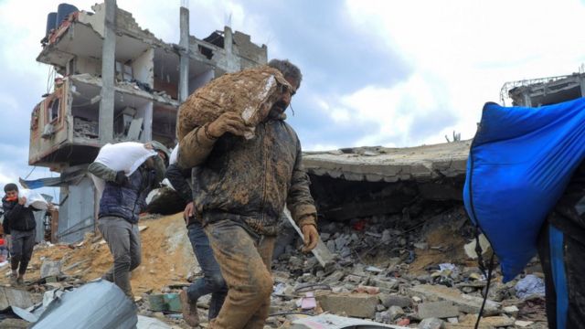援助トラックから手にした小麦粉の袋を抱えるパレスチナの人たち（27日、ガザ市）