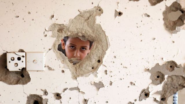 A Yemeni child looks out from behind a wall damaged in an air strike in the southern city of Taez