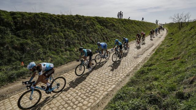 Fila de ciclistas manejando por un camino de adoquines en la carrera París-Roubaix.