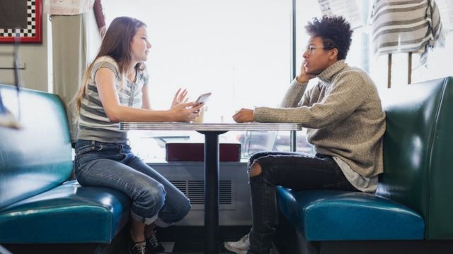 Teenage girl and boy talk in a booth at a retro cafe