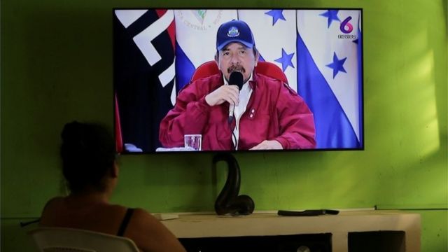 Mulher assiste à televisão, onde aparece Daniel Ortega fazendo um discurso