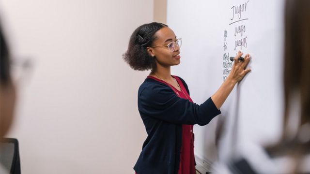 Una mujer escribe palabras en español en una pizarra.