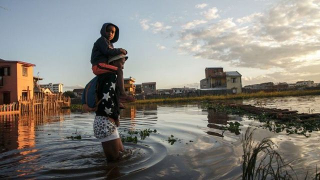 رجل يحمل طفلة ويعبر بها منطقة مغمورة بالمياه.