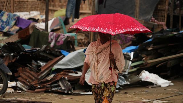 Woman with umbrella walks past damaged buildings