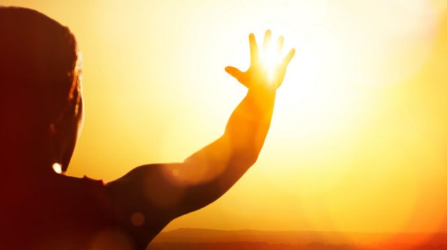 homem estendendo a mão em direção à luz do sol