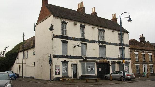 The exterior of The Old Falcon, as seen from the road in 2011. It is a cream building with black stripes running horizontally. The windows are boarded up and a car is parked outside. It looks run down.