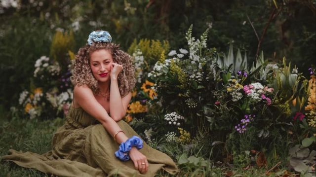 Chloe sentada em um jardim e sorrindo em direção à câmera