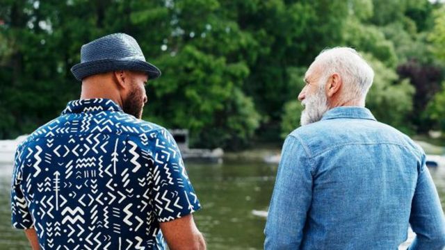 Um homem mais velho e um rapaz se olhando enquanto conversam em frente a lago 