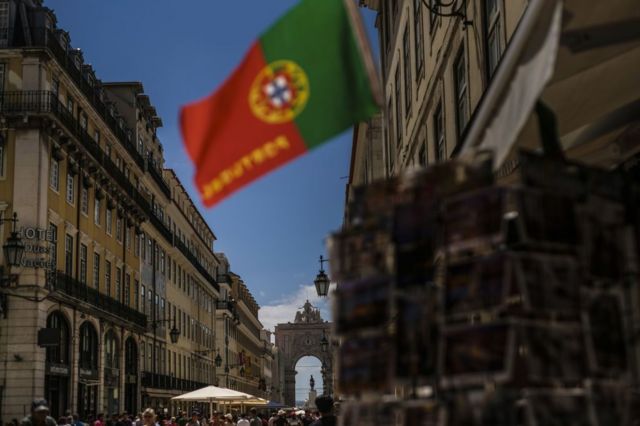 Rua em Lisboa cheia de gente com bandeira de Portugal no alto