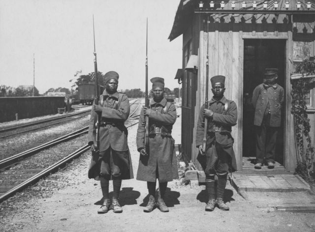 Three African soldiers from a unit of the Batallon Tirailleurs Sénégalais of the Colonial Infantry of the French army with their rifles.  They are on guard at a station in France circa June 1915