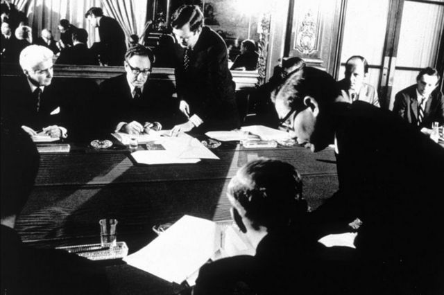 Assis autour d'une table, Henry Kissinger, alors secrétaire d'État américain, Le Duc Tho, politicien et général nord-vietnamien, signent des documents