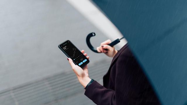 Pessoa de guarda-chuva olhando para celular com previsão do tempo