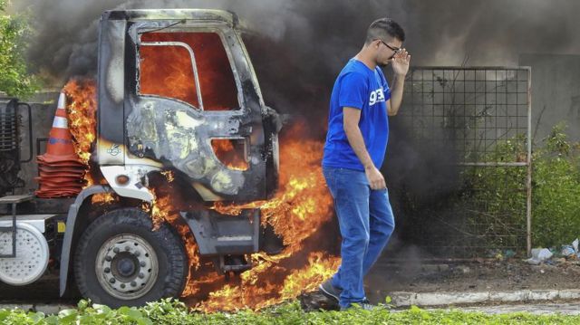 Homem caminhando ao lado de caminhão pegando fogo