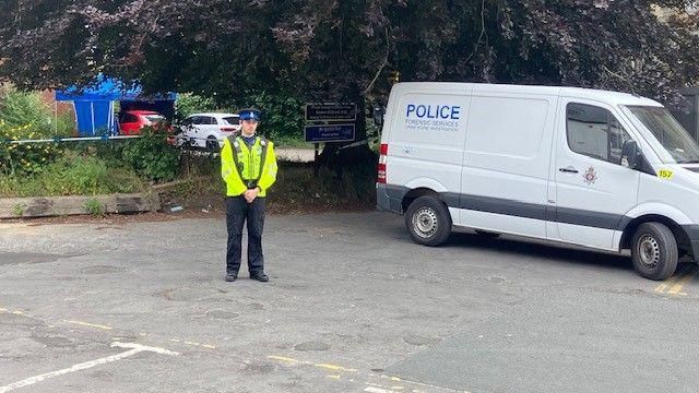 A police officer standing in the car park next to a police van