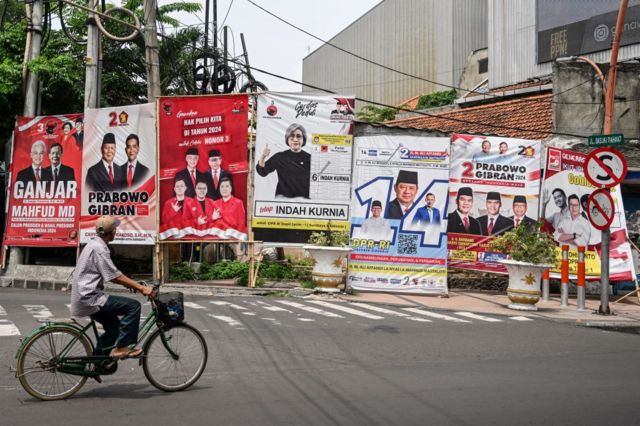Seorang pria mengendarai sepedanya melewati baliho jelang pemilu Indonesia pada 14 Februari.