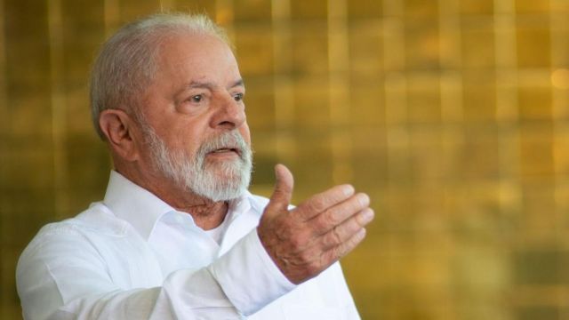 Lula, atual presidente do Brasil, veste uma camisa branca e gesticula com a mão