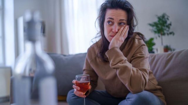 Mulher com cara de preocupação com copo de vinho na mão