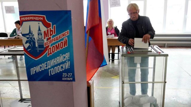 M﻿ariupol'deki referandumdan bir kare. Afişte "Eve geri dönüyoruz, katılın, oy verin" yazıyor. 