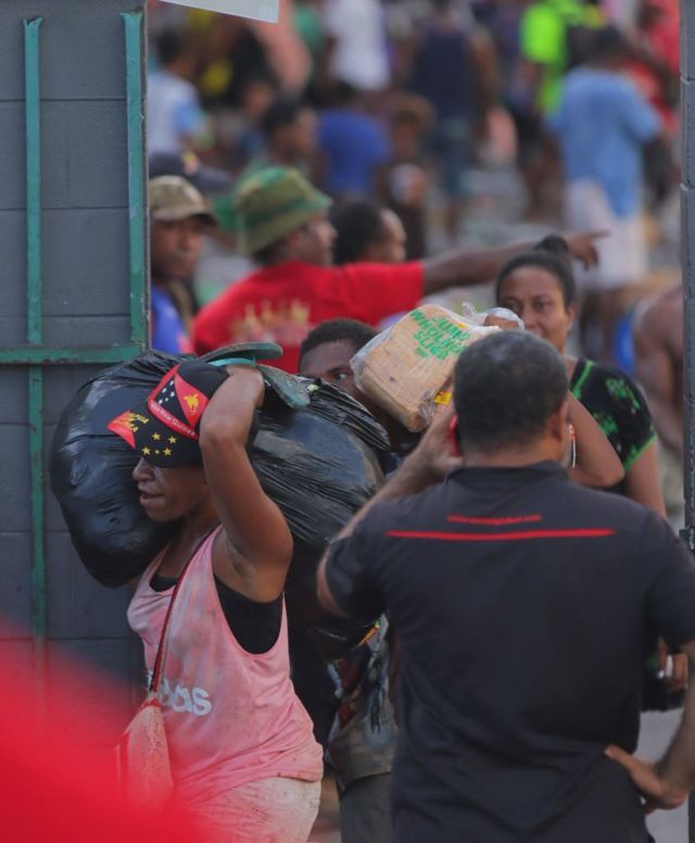 Orang-orang membawa barang-barang saat massa meninggalkan toko-toko dengan barang-barang jarahan di tengah kerusuhan di Port Moresby, Rabu, 10 Januari 2024.