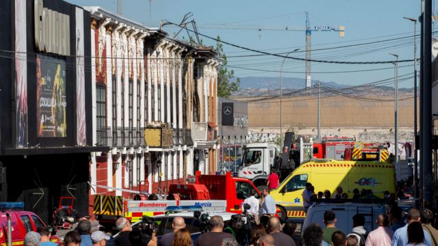 pessoas e carros de bombeiro em frente ao local do incêndio