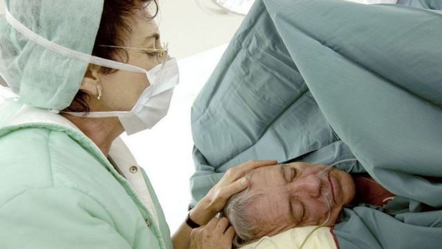 Mulher de máscara colocando a mão sobre a cabeça de paciente sedado - cirurgia sob hipnose na Bélgica
