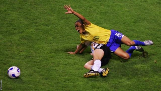 Marta gritando enquanto cai no gramado, em disputa por bola com jogadora da Alemanha