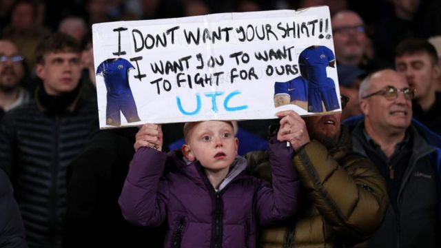 Chelsea fan holds up sign saying 'I don't want your shirt I want you to fight for ours'