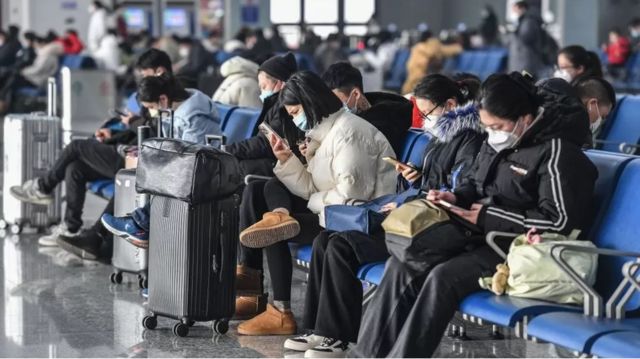Hành khách đeo khẩu trang và xem điện thoại tại một ga tàu ở Trung Quốc 