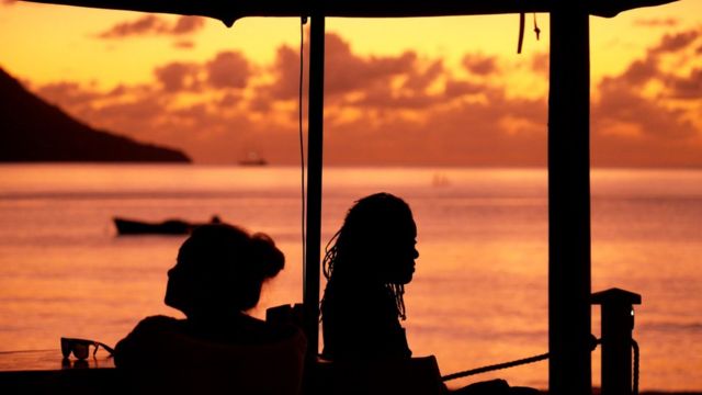 Imagem mostra duas pessoas contra a luz e o mar de Seychelles