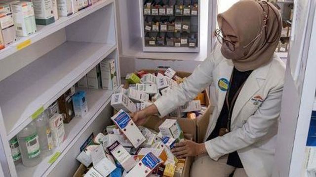 Seorang apoteker mengosongkan rak berisi sirup di apotek. 
