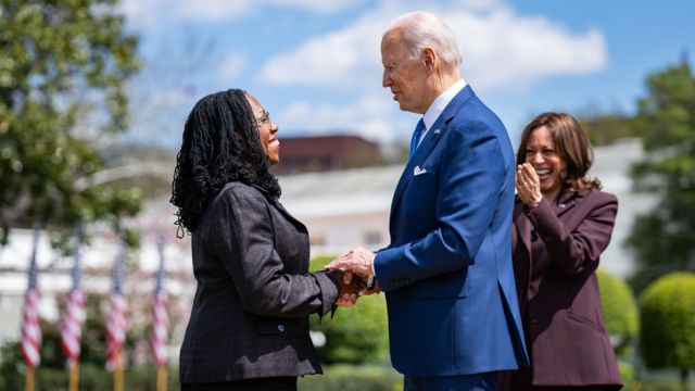 Joe Biden e Jackson apertando as mãos e sorrindo ao trocar olhares em cerimônia