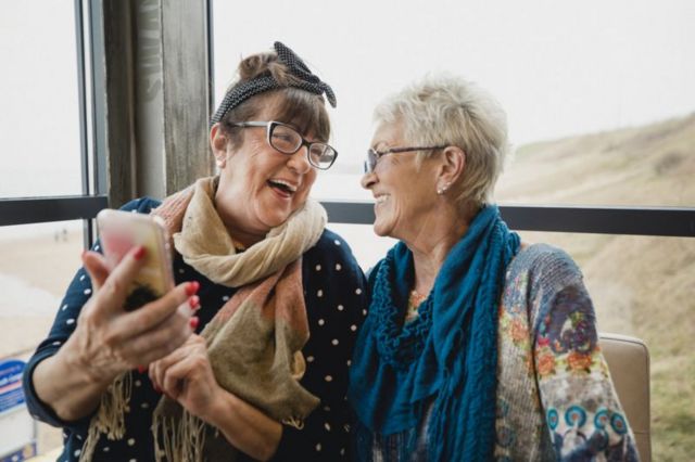 Idosas sorriem enquanto olham para o celular