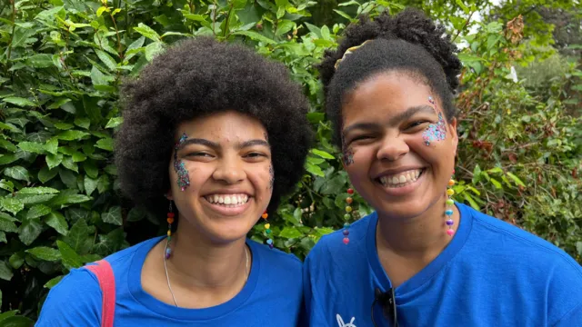 Dolly Kombate (left) and Liz Kombate (right) wear blue Mind t-shirts and smiling with glitter on their faces.