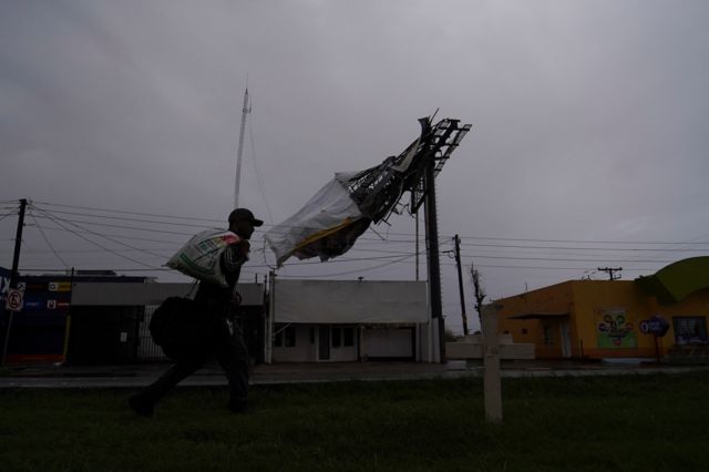 Un hombre pasa junto a una valla publicitaria colapsada por la tormenta tropical Hilary, que golpea el estado de Baja California, en Mexicali, México.