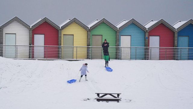 Дети катаются на санках у пляжных домиков на побережье Нортумберленда 