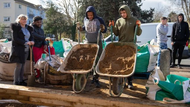 Dois jovens fazendo trabalho voluntário com carrinhos de mão cheios de terra via Timebanking UK