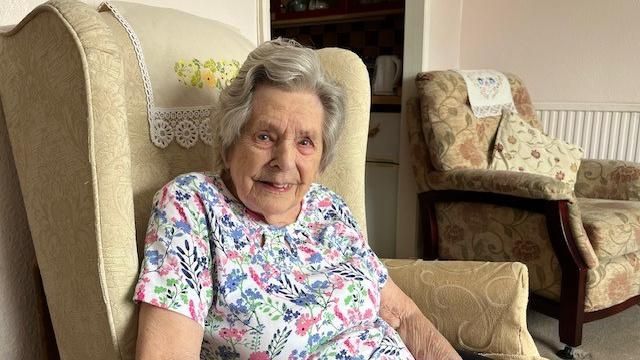 Kath Gaisford sits in an arm chair at home