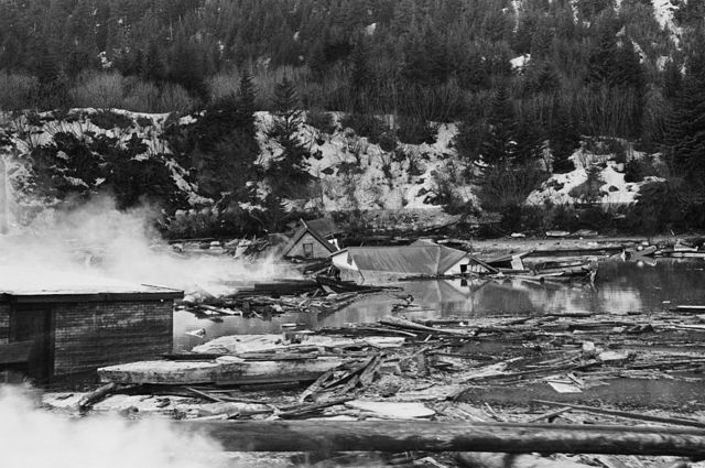 Humo de los restos de tanques de petróleo entre las ruinas de casas después del terremoto y tsunami de Alaska