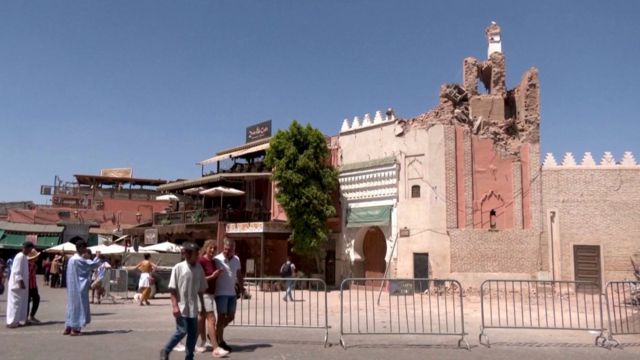 Turistler ve yerel halk, depremin ardından hasar gören Jemaa el-Fna minaresinin önünden geçiyor