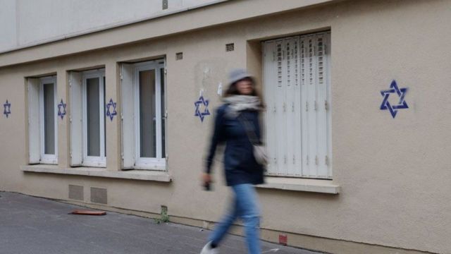 Una mujer camina frente a una fachada pintada con estrellas de David en París