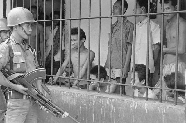 Seorang anggota militer Indonesia mengawasi beberapa orang yang dicurigai sebagai anggota atau simpatisan PKI di Tangerang, usai 1 Oktober 1965.