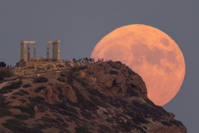 La gente observa la superluna azul saliendo en el Templo de Poseidón, cerca de Atenas, Grecia.