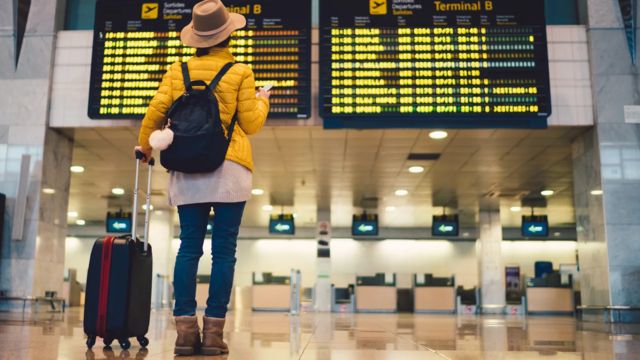 Mulher em aeroporto olhando as previsões de embarque de voos