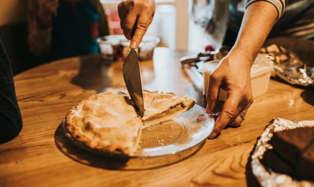 Pessoa cortando torta na mesa, aparentemente em festa 